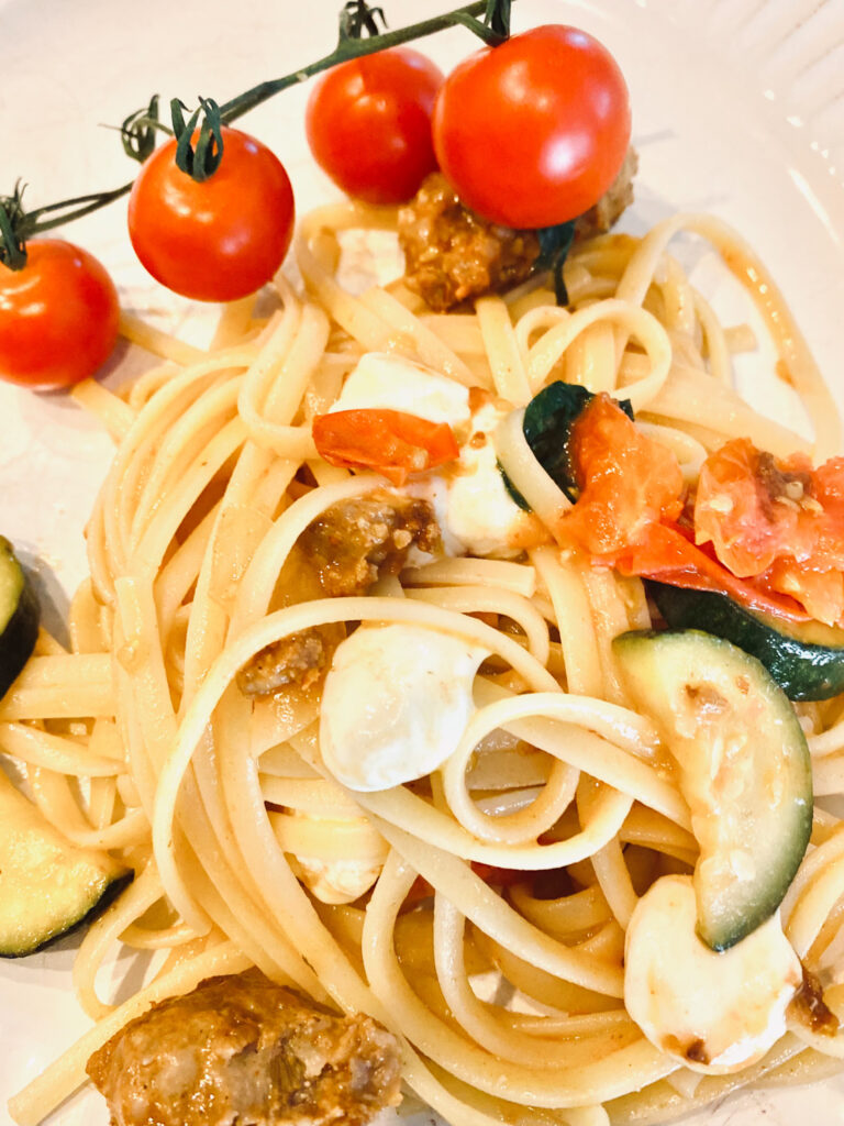 Pasta with zucchini, cherry tomatoes, Italian sausage and fresh mozzarella on a white plate. 