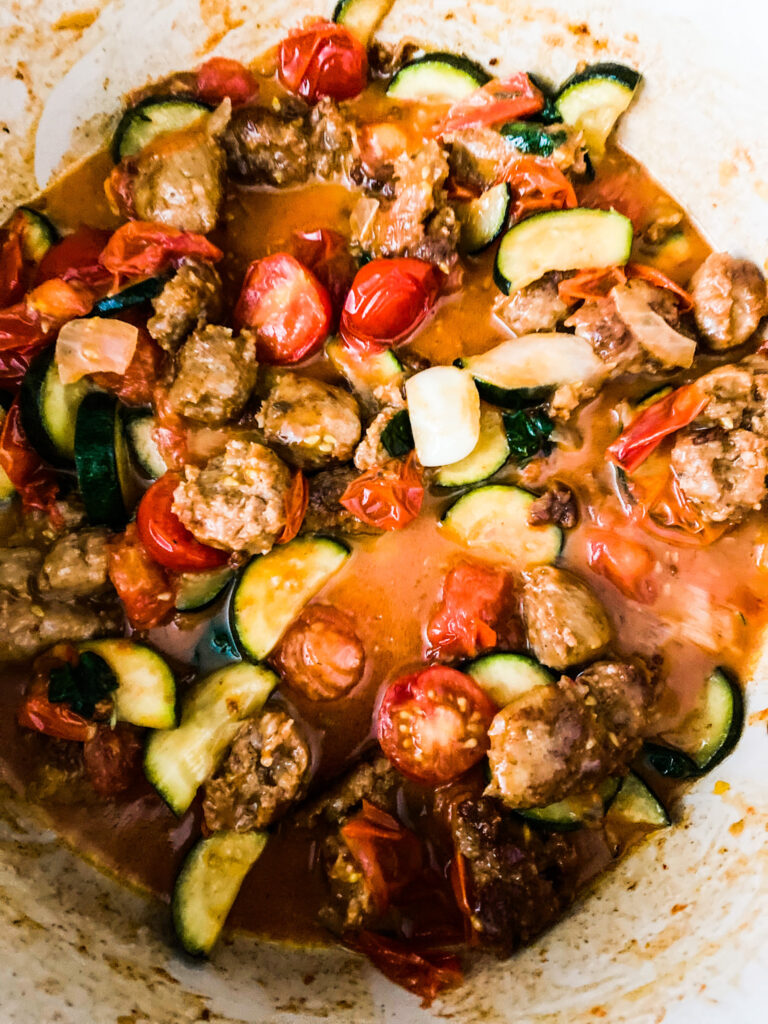 Zucchini in quarters, with halved cherry tomatoes, and Italian sausage with onions diced in a large pot on the stove. 