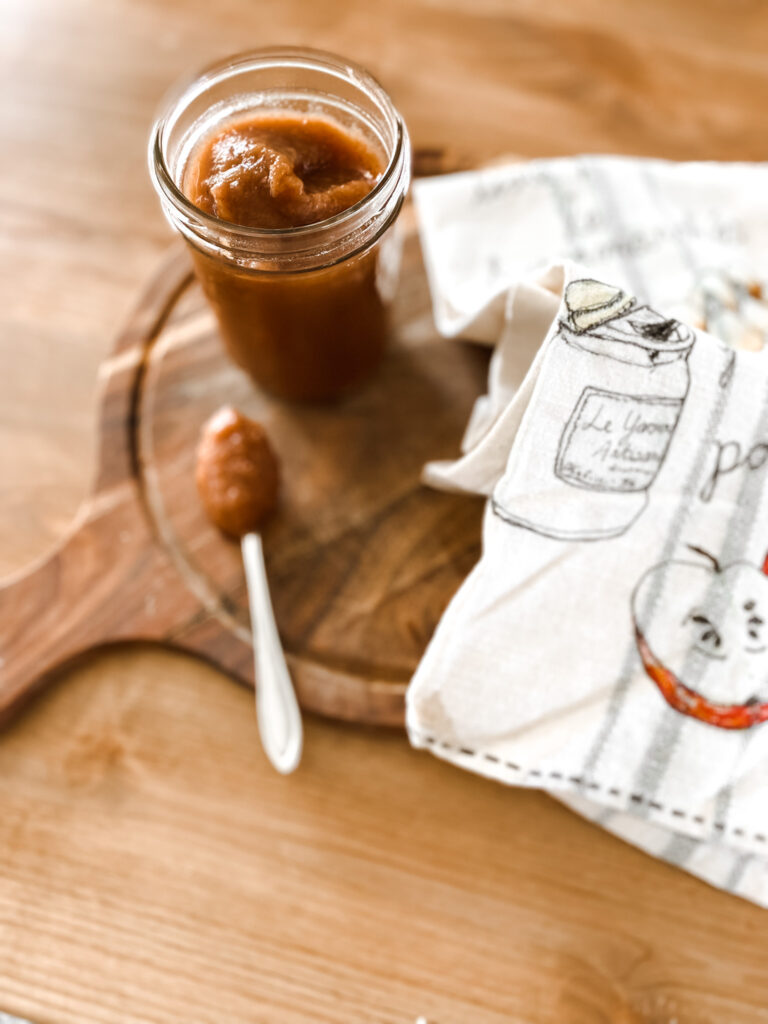 Apple sauce in a jar with a spoon and tea towel on a cutting board