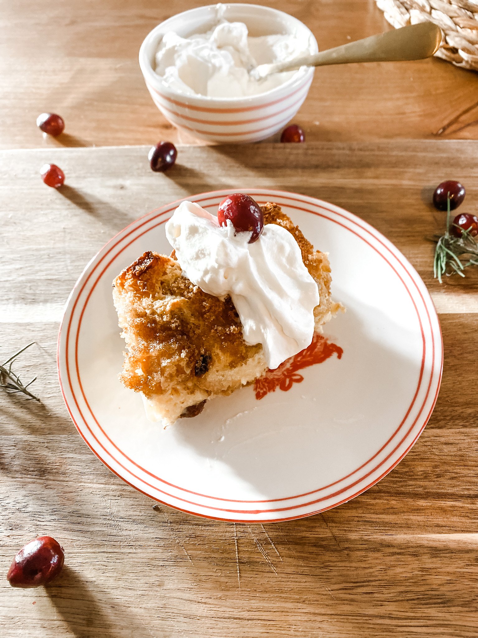 Baked French Toast slice with whipped cream and cranberries on a red and white plate