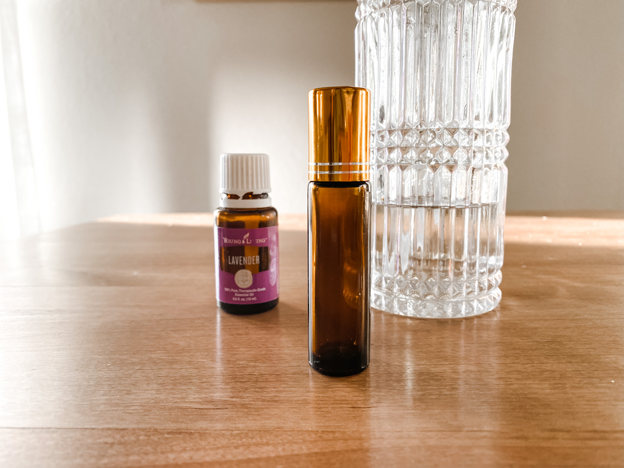 Essential Oil Roller Ball next to Lavender essential oil and crystal carrier oil dispenser on a wood table.