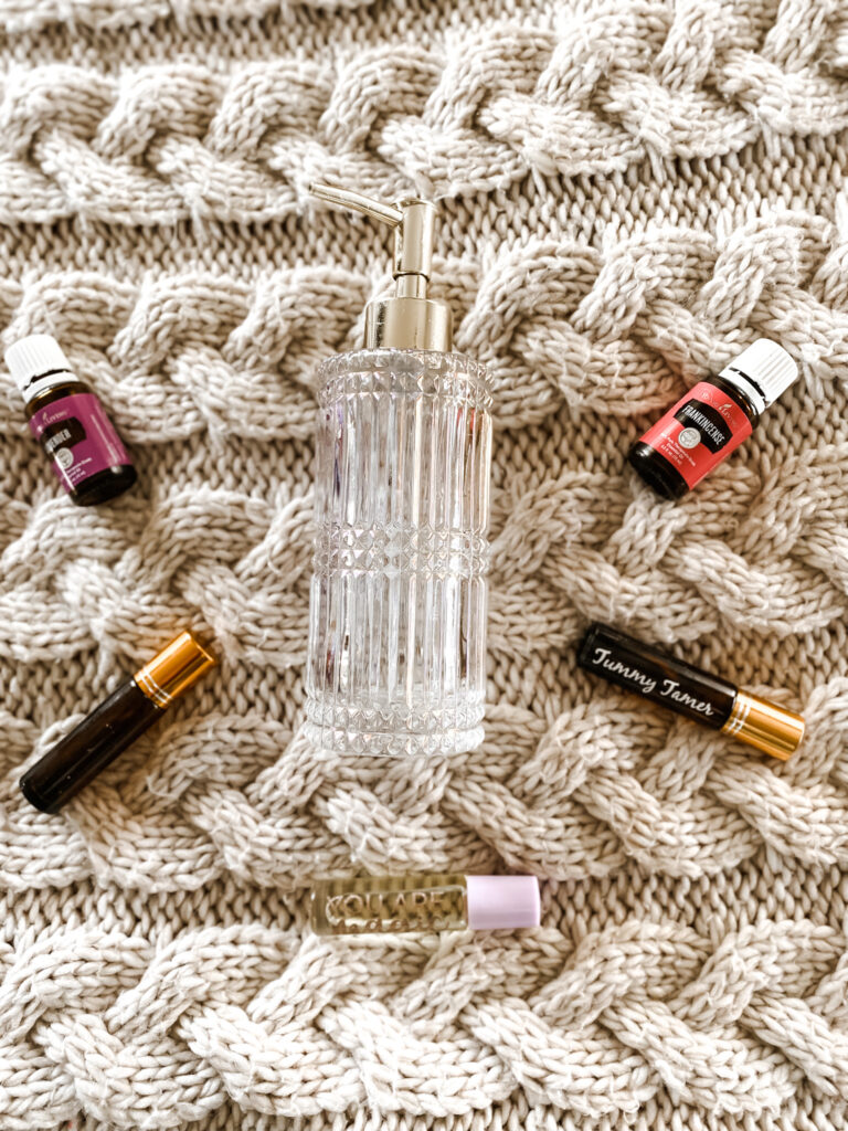 Crystal carrier oil dispenser with essential oil roller balls, essential oil lavender, and essential oil frankincense on a white knit blanket. 