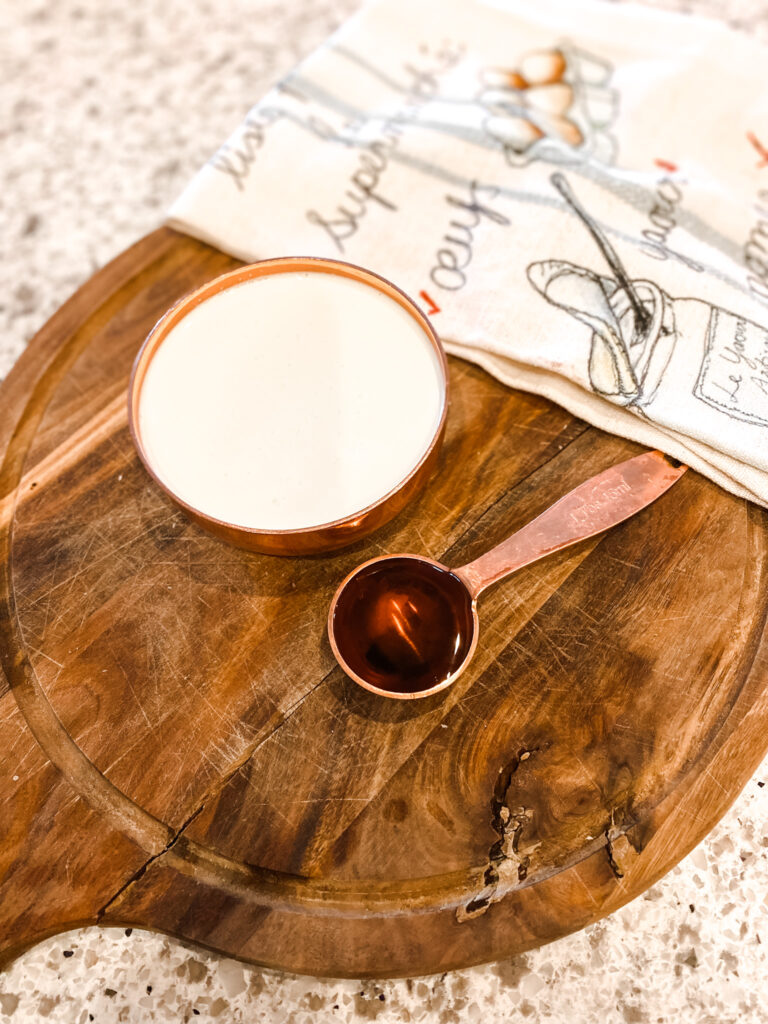 Cup of heavy cream, maple syrup on a wood cutting board next to a tea towl. 