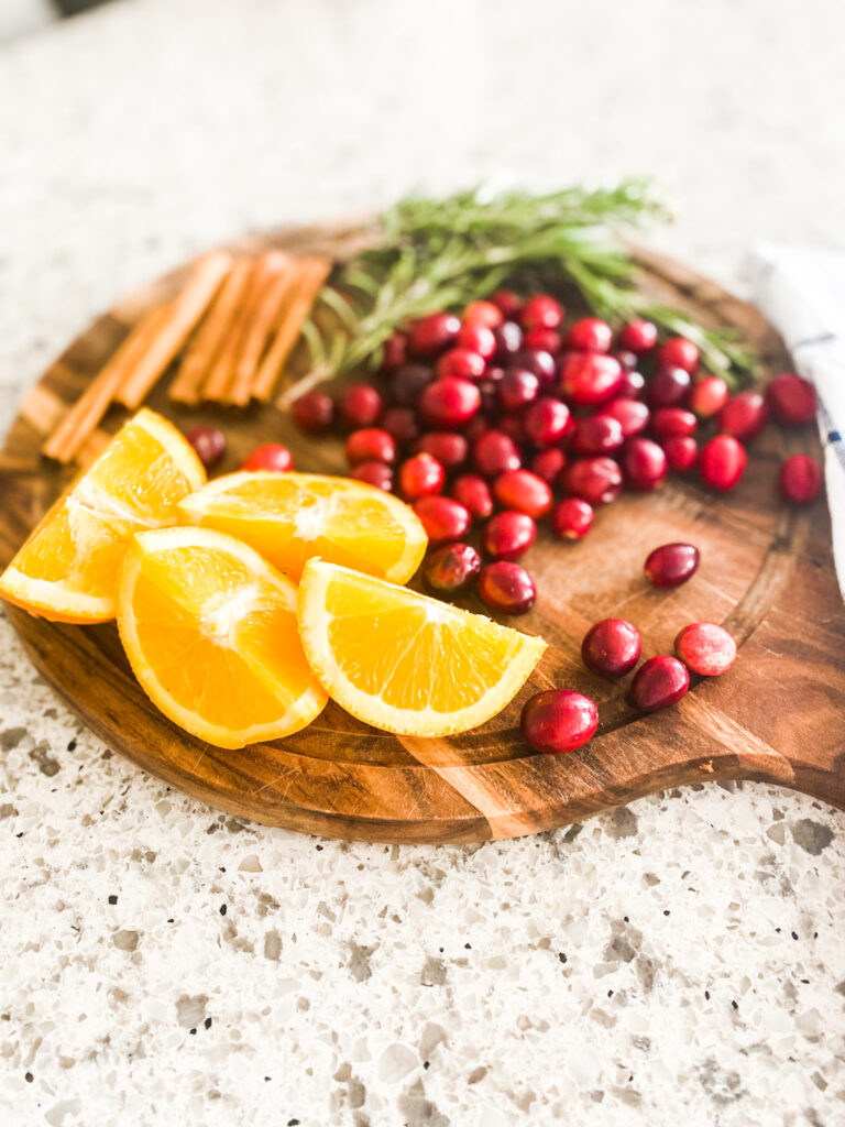 Orange slices, cinnamon sticks, sprigs of rosemary and cranberries on a wood cutting board