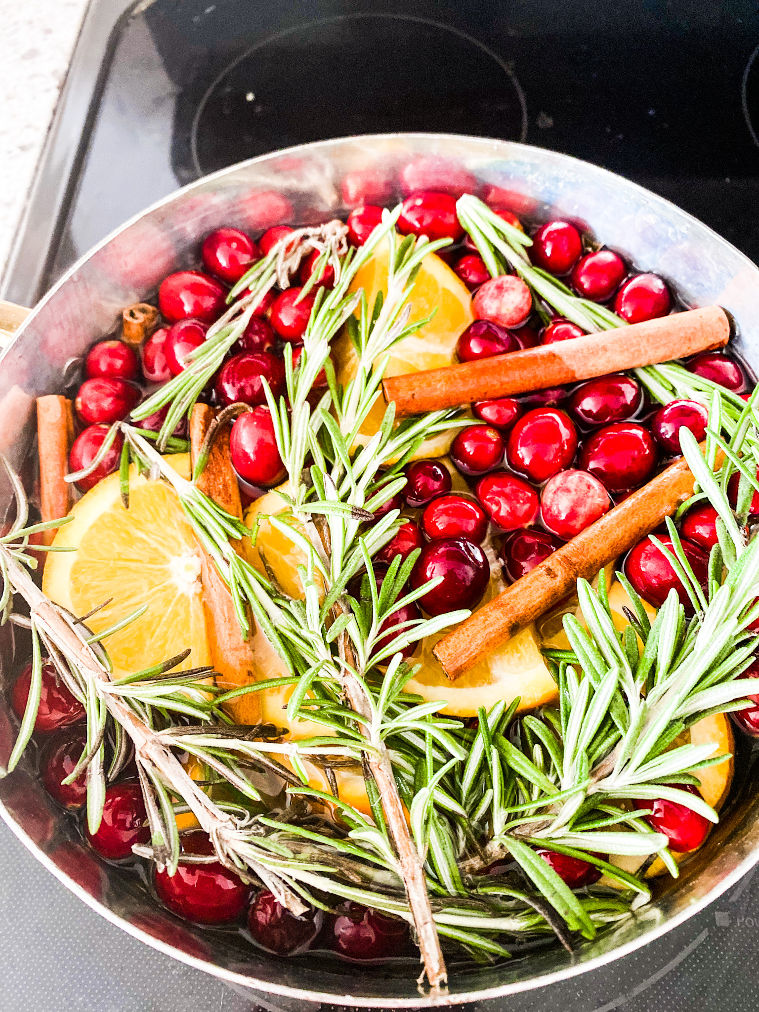 Copper pot with cranberries, oranges, cinnamon sticks, and rosemary