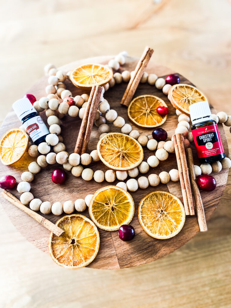 Dried orange slices, cinnamon sticks, cranberries, wood beads, and essential oils on a wood cake stand. 
