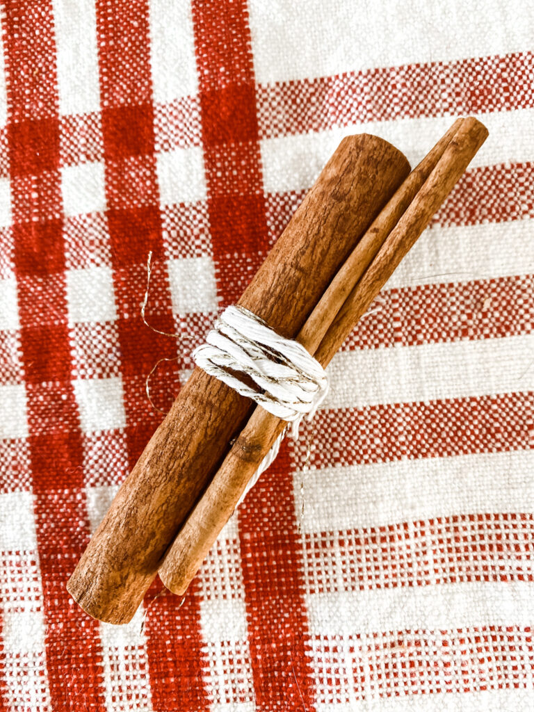 Two cinnamon sticks tied together on a white and red table cloth. 