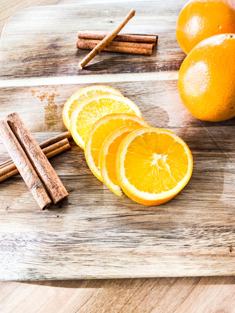 Cinnamon sticks, orange slices, and oranges on a wood cutting board