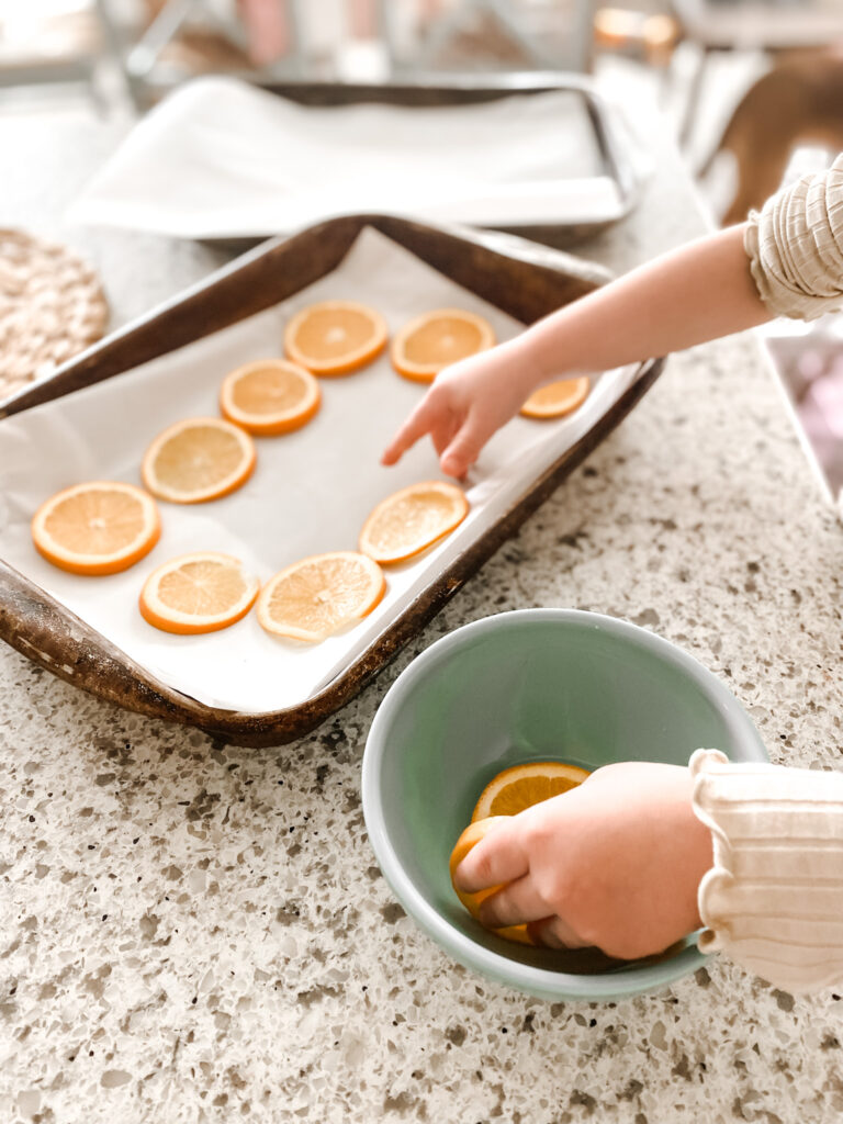 Sliced oranges being set on a baking sheet with parchment paper. 