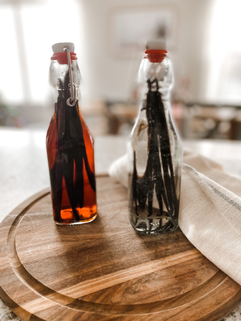 A bottle of homemade vanilla and a bottle of vanilla beans and vodka on a wood cutting board. 