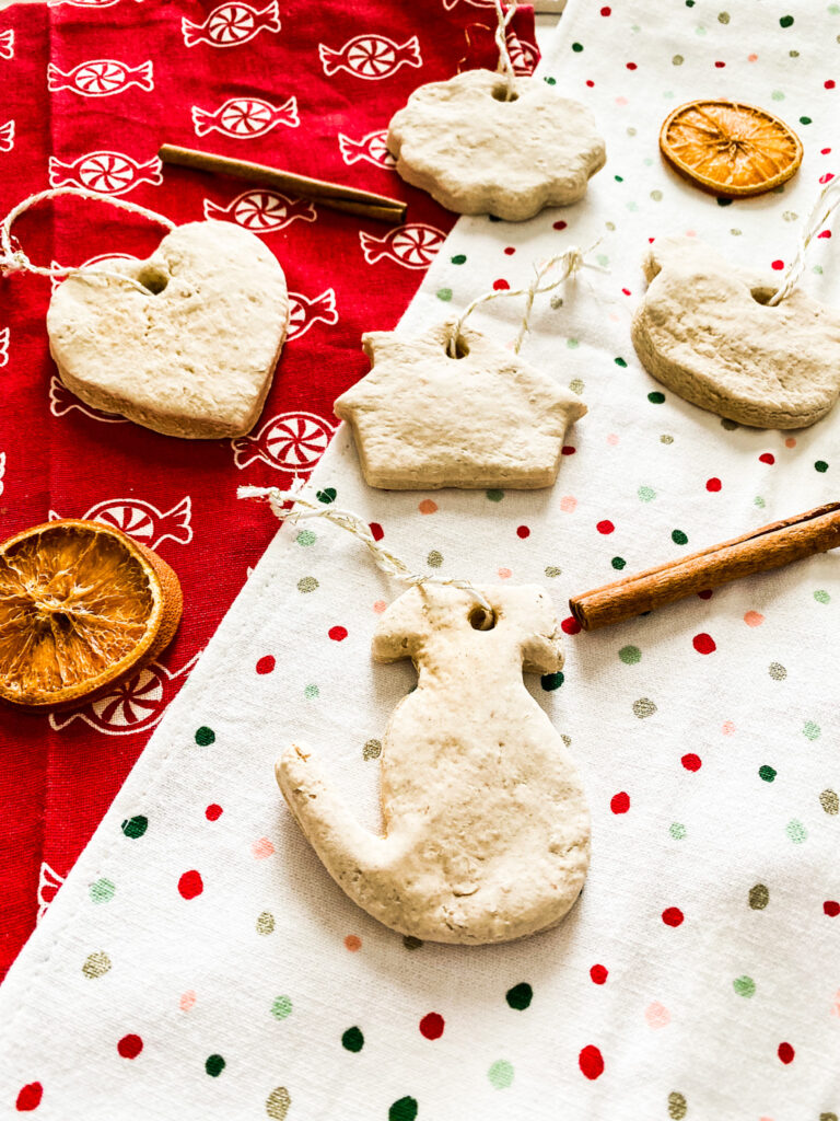 Salt dough ornaments and cinnamon sticks and dried orange slices on a holiday tea towel. 