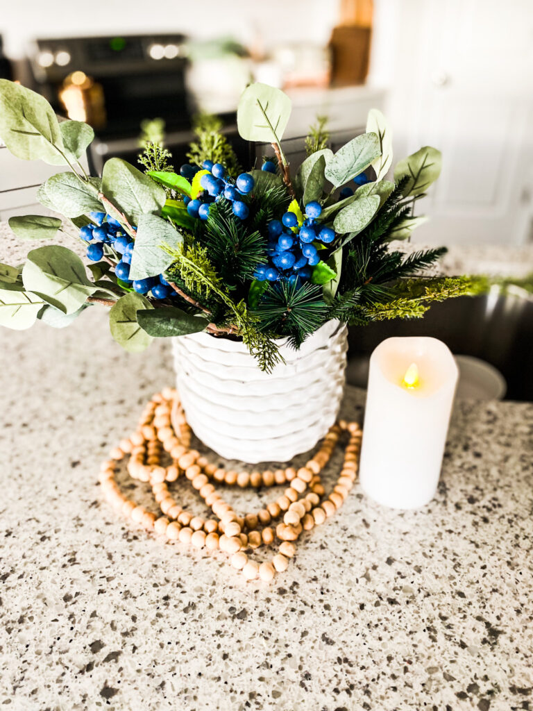 Greenery in a white pot with wood beads and a flameless candle. 