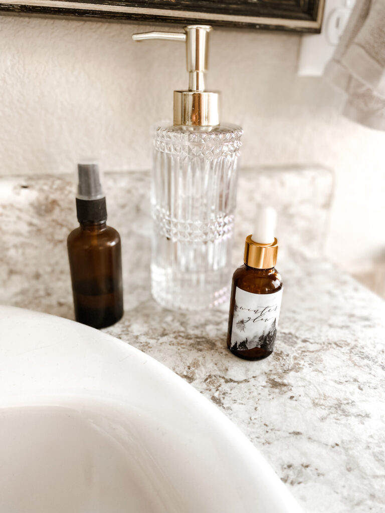 Ember spray bottle, glass bottle, and glow serum bottle on a bathroom counter. 