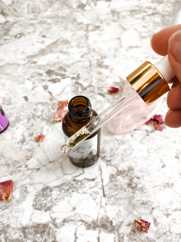 Glow serum for natural skincare in a dropper bottle on a bathroom counter with pink rose petals. 