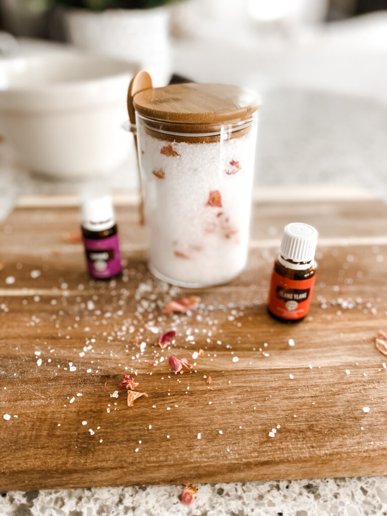 bath salts with essential oils and rose petals in a jar on a wood cutting board