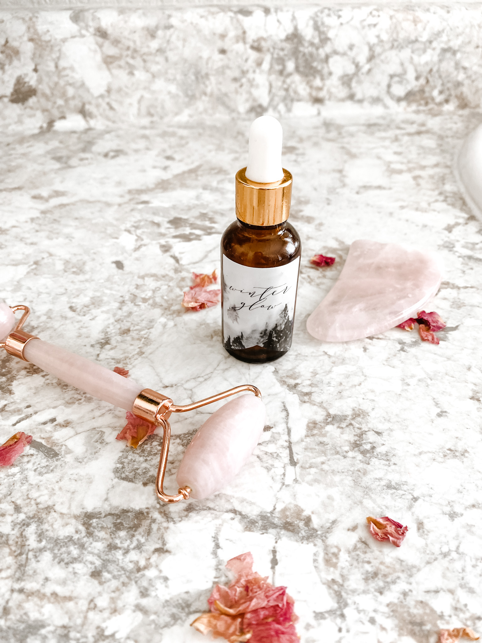 Glow Serum for natural skincare next to a rose quartz roller and pink rose petals.