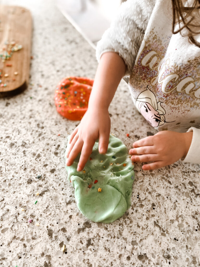 Child mixing green and white homemade playdough with sprinkles on a counter