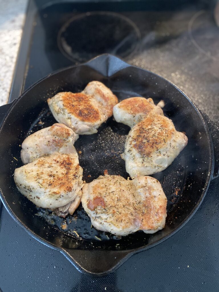 four cooked and seasoned chicken thighs in a cast iron skillet on a stove