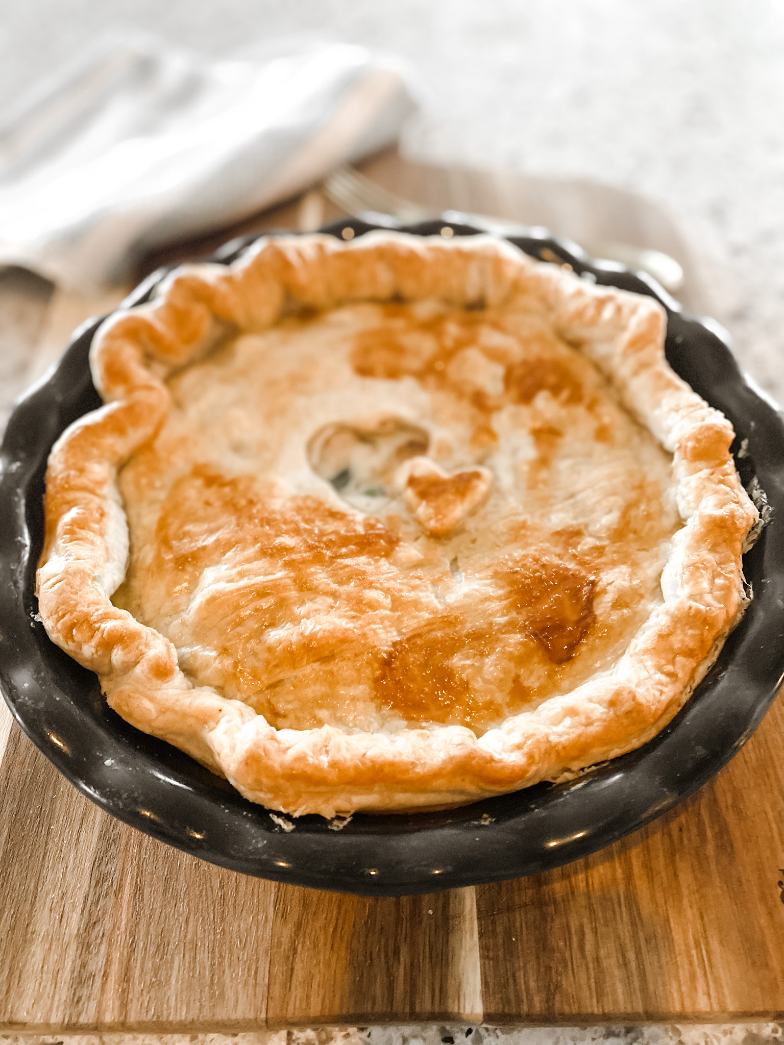 baked chicken pot pie in a round blue baking dish on a wood cutting board