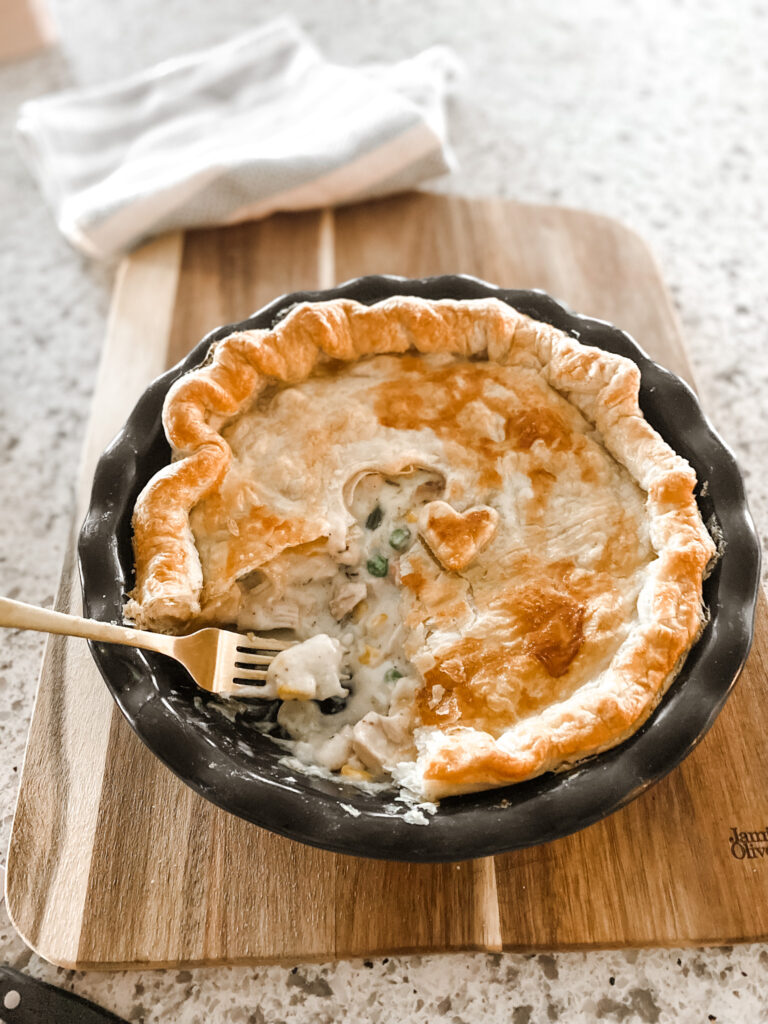 Part of a cooked chicken pot pie in a round blue baking dish with a gold fork on a wood cutting board