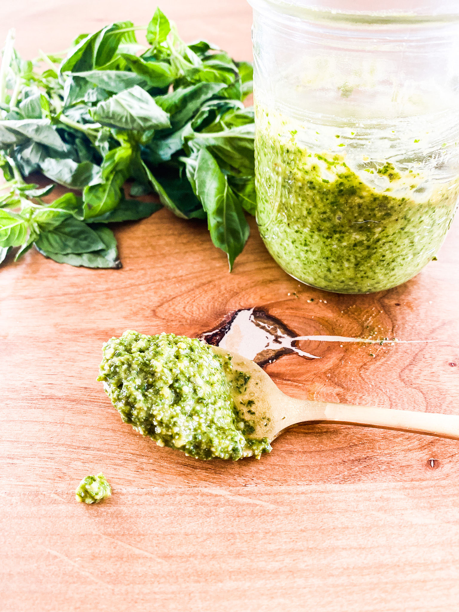 Homemade Pesto Sauce in a jar and on a gold spoon on a wood table in front of fresh basil
