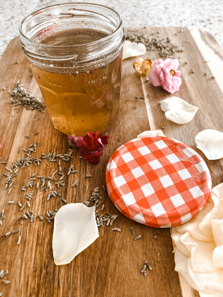 Jar of lavender simple syrup on a wood cutting board with lavender buds and flower petals