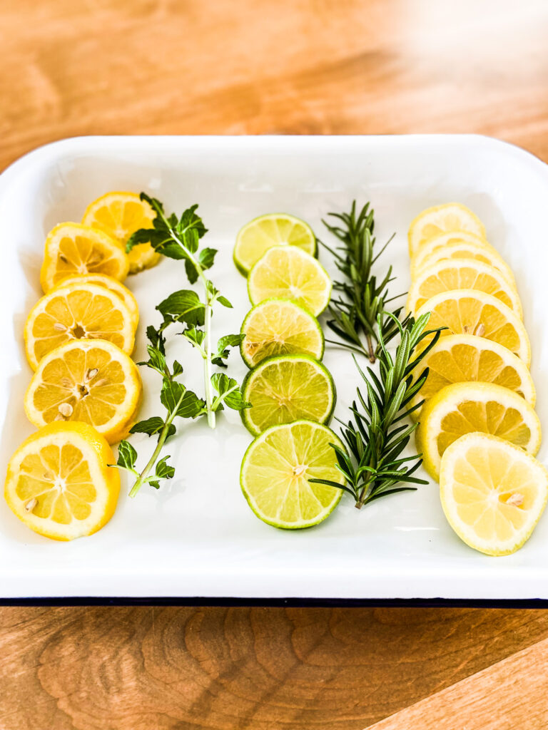White tray of lemon slices, lime slices, fresh mint and fresh rosemary. 