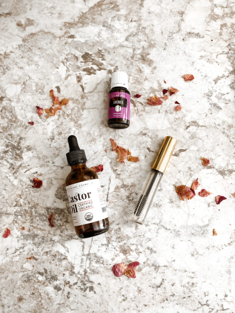 lash boost serum DIY in a mascara tube on a counter with a  lavender essential oil, castor oil, and pink rose petals
