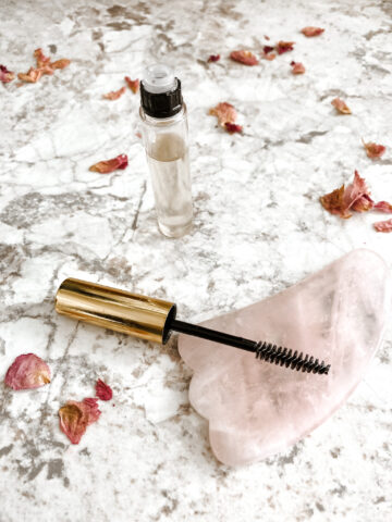 lash boost serum DIY in a mascara tube on a counter with a rose quartz stone and pink rose petals