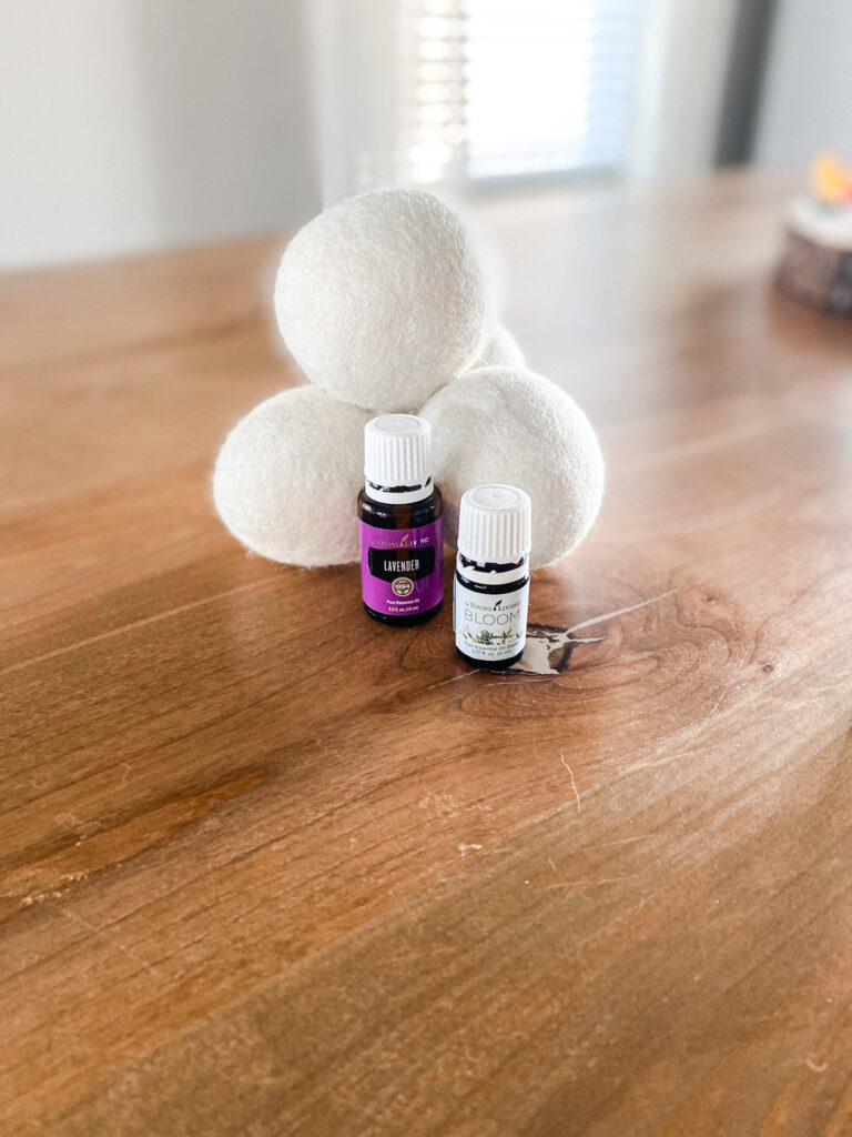 4 wool dryer balls on a wood table behind lavender and bloom essential oil. 