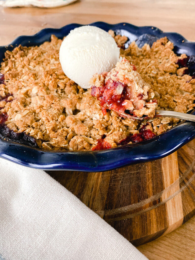 summer berry crisp in a blue baking dish with vanilla ice cream on top