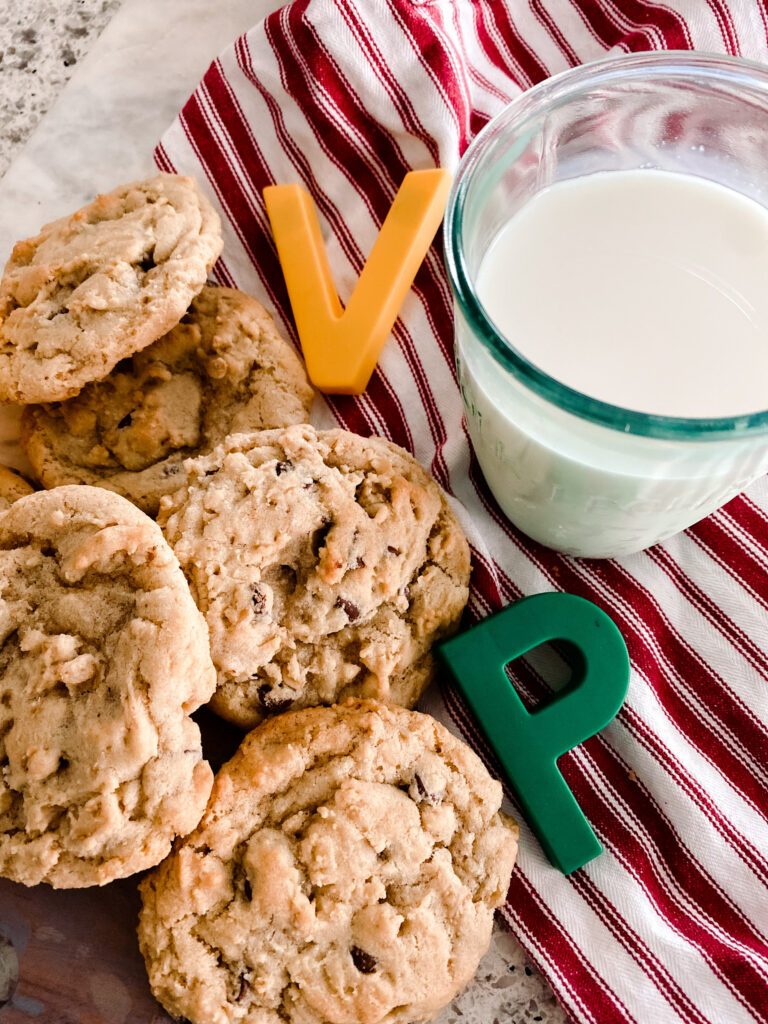 oatmeal chocolate chip cookies next to a glass of milk on a red and white stripe towel with green and yellow letters