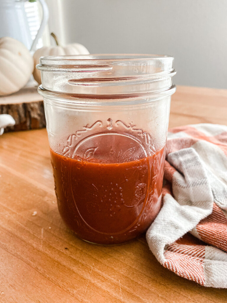 homemade BBQ sauce in a mason jar on a wood table next to a gray and rust colored towel. 
