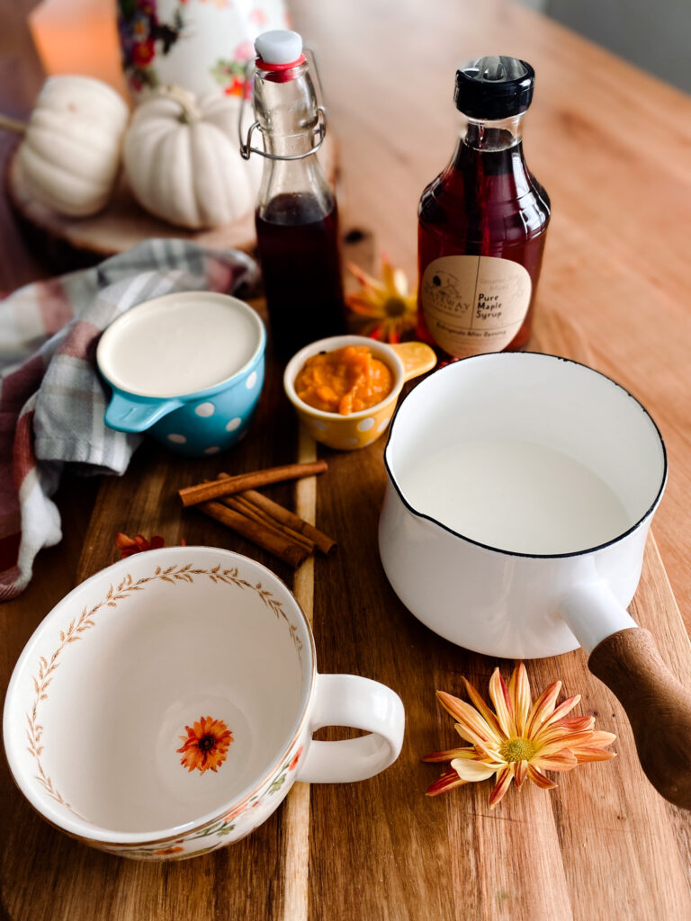 Heavy cream, milk, pumpkin puree, cinnamon sticks, vanilla extract and maple syrup on a wood table. 