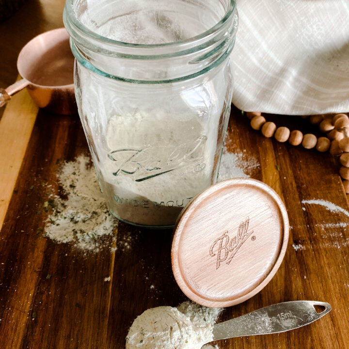 mason jar on a wood cutting board with homemade ranch seasoning in it and on a spoon next to the jar.