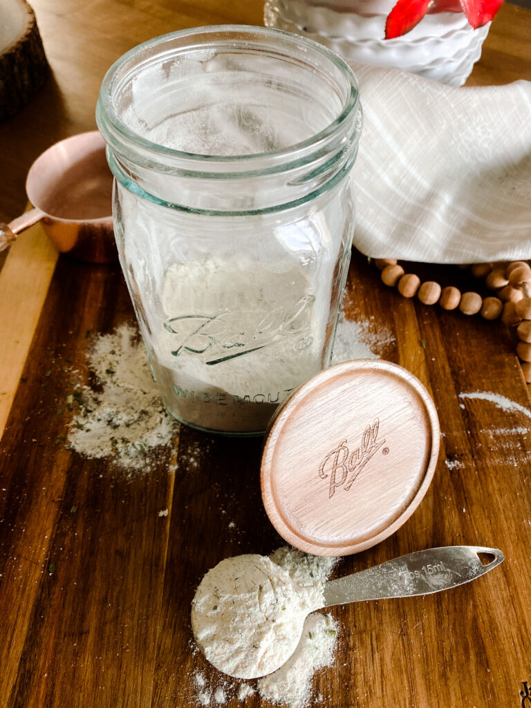 mason jar on a wood cutting board with homemade ranch seasoning in it and on a spoon next to the jar.