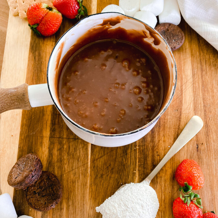 homemade chocolate fondue in a white pot next to strawberries, marshmallows, and brownie bites