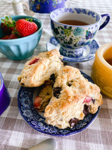 strawberry scones with chocolate chunks on a blue and white tea dish next to strawberries and honey, and tea