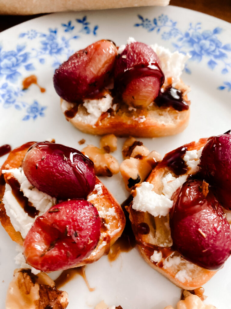 roasted grapes appetizer with goat cheese and walnuts on a blue and white floral plate